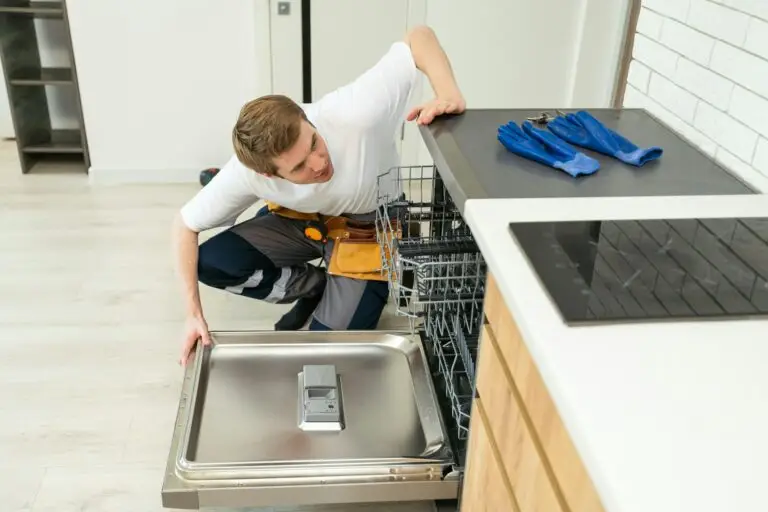 Technician or worker in uniform installs dishwasher into the kitchen furniture. Repairman wear